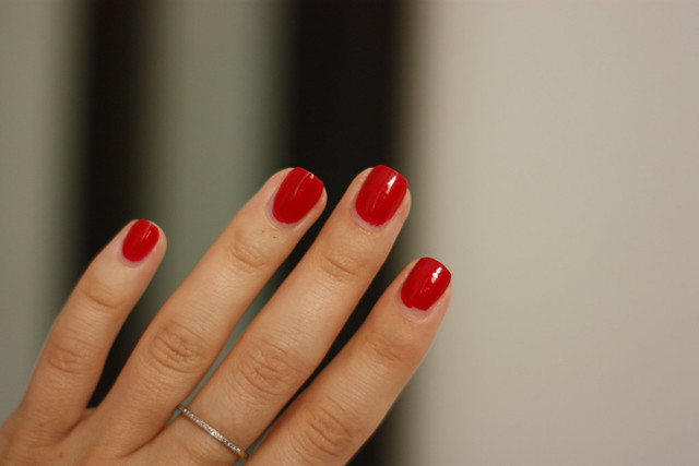Close-up of a hand with glossy red nail polish and a thin ring, neutral blurred background