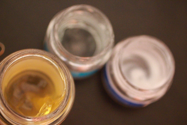 Close-up of three open small jars with liquid or residue inside, viewed from above, in warm brown and amber tones, blurred background